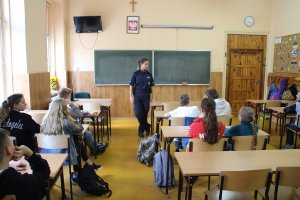 Zdjęcie przedstawia umundurowaną policjantkę prowadzącą w sali lekcyjnej zajęcia dla siedzących w klasie uczniów.