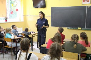 Zdjęcie przedstawia umundurowaną policjantkę prowadzącą w sali lekcyjnej zajęcia dla siedzących w klasie uczniów.