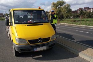 Zdjęcie przedstawia policjanta ruchu drogowego kontrolującego dostawcze auto koloru żółtego.