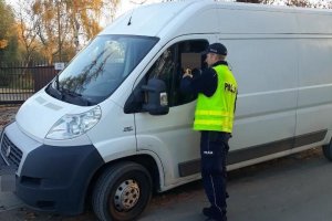 Zdjęcie przedstawia umundurowanego policjanta prowadzącego kontrolę trzeźwości kierowcy auta dostawczego.