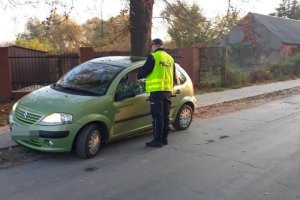 Zdjęcie przedstawia umundurowanego policjanta prowadzącego kontrolę trzeźwości kierowcy auta osobowego.