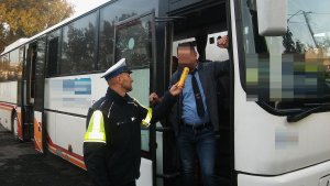 Zdjęcie przedstawia umundurowanego policjanta prowadzącego kontrolę trzeźwości kierowcy autobusu