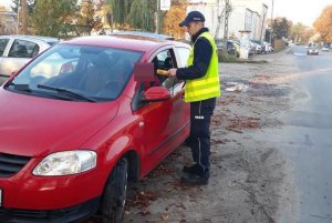 Zdjęcie przedstawia umundurowanego policjanta prowadzącego kontrolę trzeźwości kierowcy auta osobowego.