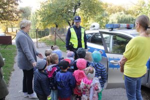 Zdjęcie przedstawia umundurowanego policjanta stojącego razem z dziećmi i opiekunami koło radiowozu.