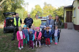 Zdjęcie przedstawia dzieci stojące razem z opiekunkami i umundurowanymi policjantami pozujących do fotografii.