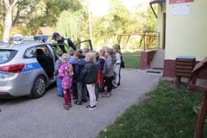 Zdjęcie przedstawia dzieci stojące przy radiowozie i oglądające go. Razem z dziećmi stoi umundurowany policjant.