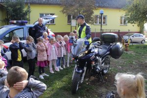 Zdjęcie przedstawia dzieci stojące obok służbowego motocykla i radiowozu. z dziećmi stoi dwóch policjantów.