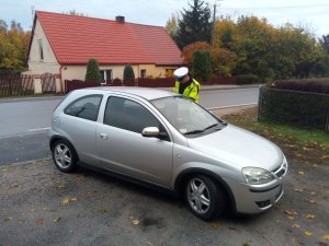 Zdjęcie przedstawia policjanta ruchu drogowego kontrolującego auto osobowe.