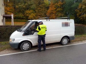 Zdjęcie przedstawia policjanta ruchu drogowego kontrolującego auto dostawcze.