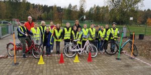 Zdjęcie przedstawia dzieci biorące udział w egzaminie na kartę rowerową wspólnie z umundurowaną policjantką i opiekunem