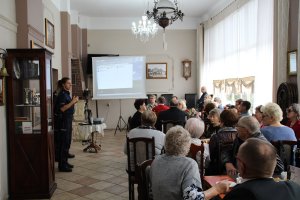 Zdjęcie przedstawia policjantkę prowadzącą zajęcia dla Seniorów siedzących w sali