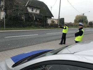 Zdjęcie przedstawia dwóch policjantów ruchu drogowego, z których jeden mierzy prędkość pojazdów.