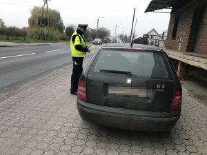 Zdjęcie przedstawia policjanta ruchu drogowego kontrolującego auto osobowe.