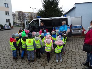 Zdjęcie przedstawia policjantkę, dzieci i ich opiekunkę stojących obok policyjnego oznakowanego radiowozu.