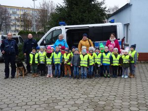 Zdjęcie przedstawia policjantkę, policjanta, dzieci i ich opiekunki pozujących na tle oznakowanego radiowozu do wspólne fotografii.