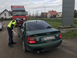 Zdjęcie przedstawia umundurowanego policjanta ruchu drogowego kontrolującego pojazd osobowy