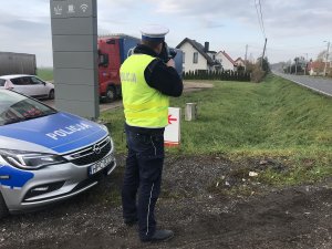 Zdjęcie przedstawia umundurowanego policjanta ruchu drogowego mierzącego prędkość aut laserem