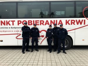 Zdjęcie przedstawia policjantów, którzy włączyli się w akcję. Mundurowi stoją przy autobusie do odbioru krwi.