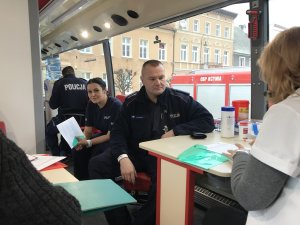 Zdjęcie przedstawia policjantów, którzy włączyli się w akcję. Mundurowi siedzą w autobusie do odbioru krwi i wypełniają niezbędną dokumentację.