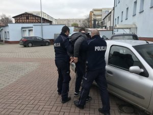 zdjęcie przedstawia osobę zatrzymaną prowadzoną przez policjantów