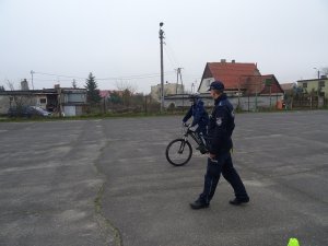 Zdjęcie przedstawia umundurowanego policjanta nadzorującego chłopca zdającego praktyczny egzamin na kartę rowerową.