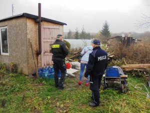 Zdjęcie przedstawia umundurowanego policjanta wspólnie ze strażnikiem miejskim oraz pracownicą MGOPS prowadzących kontrole miejsc przebywania bezdomnych.