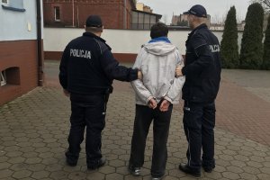 Zdjęcie przedstawia podejrzanego prowadzonego przez policjantów