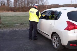 Zdjęcie przedstawia umundurowanego policjanta ruchu drogowego kontrolującego trzeźwość kierowcy auta osobowego