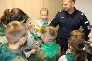 Umundurowany policjant oprowadza harcerzy po pomieszczeniach w komisariacie