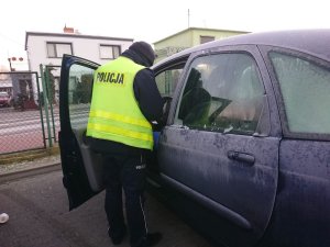 Zdjęcie przedstawia umundurowanego policjanta kontrolującego przy szkole auto osobowe