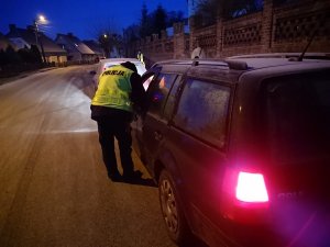 Zdjęcie przedstawia umundurowanego policjanta kontrolującego przy przedszkolu auto osobowe