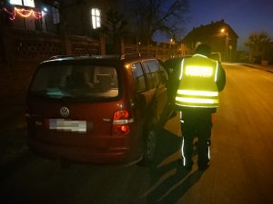 Zdjęcie przedstawia umundurowanego policjanta kontrolującego przy przedszkolu auto osobowe