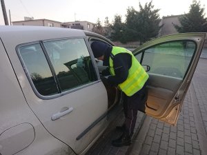 Zdjęcie przedstawia umundurowanego policjanta kontrolującego przy szkole auto osobowe