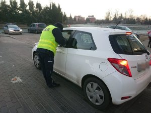 Zdjęcie przedstawia umundurowanego policjanta kontrolującego przy szkole auto osobowe