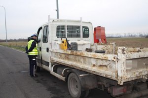 Zdjęcie przedstawia umundurowanego policjanta ruchu drogowego kontrolującego pojazd dostawczy