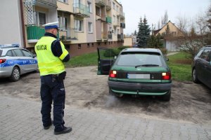 Zdjęcie przedstawia umundurowanego policjanta ruchu drogowego kontrolującego pojazd osobowy