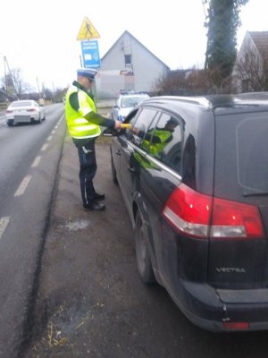 Zdjęcie przedstawia umundurowanego policjanta ruchu drogowego kontrolującego pojazd osobowy i sprawdzającego trzeźwość kierowcy.