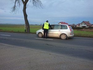 Zdjęcie przedstawia umundurowanego policjanta kontrolującego trzeźwość kierowcy pojazdu osobowego