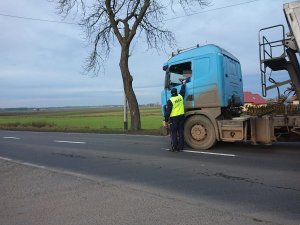 Zdjęcie przedstawia umundurowanego policjanta kontrolującego trzeźwość kierowcy pojazdu ciężarowego