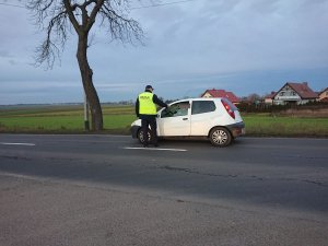 Zdjęcie przedstawia umundurowanego policjanta kontrolującego trzeźwość kierowcy pojazdu osobowego