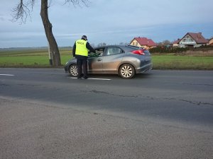 Zdjęcie przedstawia umundurowanego policjanta kontrolującego trzeźwość kierowcy pojazdu osobowego