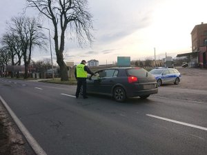 Zdjęcie przedstawia umundurowanego policjanta kontrolującego trzeźwość kierowcy pojazdu osobowego