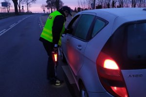 Zdjęcie przedstawia umundurowanego policjanta sprawdzającego trzeźwość kierowcy auta osobowego