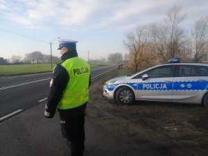 Zdjęcie przedstawia umundurowanego policjanta ruchu drogowego prowadzącego obserwację pojazdów przemieszczających się trasą.