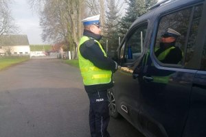 Zdjęcie przedstawia umundurowanego policjanta ruchu drogowego prowadzącego kontrolę pojazdu.