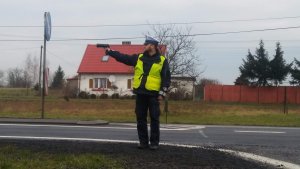 Zdjęcie przedstawia umundurowanego policjanta ruchu drogowego prowadzącego pomiar prędkości pojazdów przemieszczających się trasą.