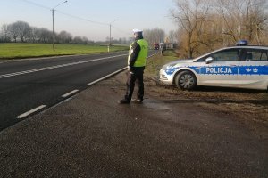 Zdjęcie przedstawia umundurowanego policjanta ruchu drogowego prowadzącego obserwację pojazdów przemieszczających się trasą.