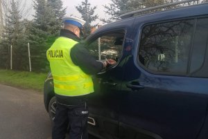 Zdjęcie przedstawia umundurowanego policjanta ruchu drogowego prowadzącego kontrolę pojazdu.