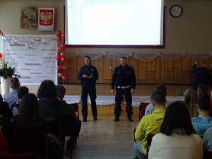 Zdjęcie przedstawia umundurowanych policjantów: kobietę i mężczyznę prowadzących zajęcia dla siedzących w auli uczniów.