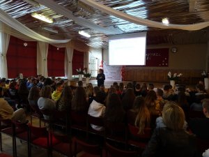 Zdjęcie przedstawia umundurowaną policjantkę prowadzącą zajęcia dla siedzących w auli uczniów.